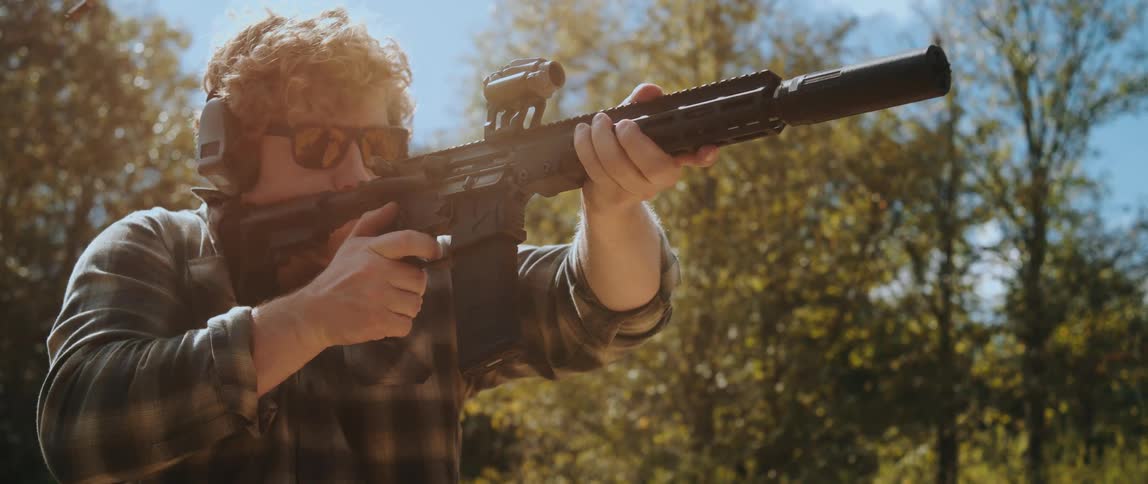 Man with a customized weapon is shooting in an environment with trees in the background