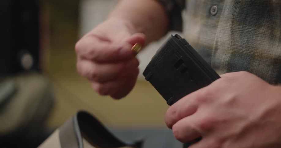 Closeup of hands loading a bullet into a handgun magazine
