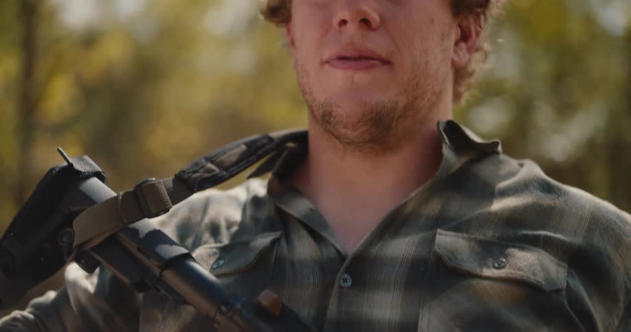 A large man holding an assault rifle stands and poses with it