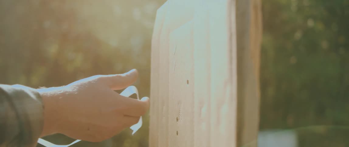 A close view of a mans hands applying a piece of white tape to a cardboard target with bullet holes in a sunny forest
