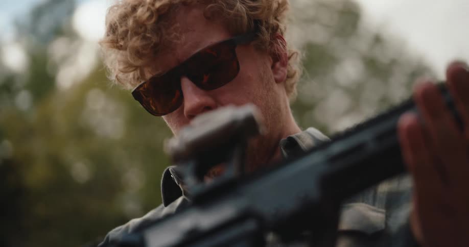 Man stands holding an automatic rifle and looks at the weapon