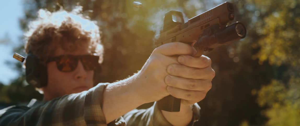 A man wearing sunglasses fires a single bullet from a handgun