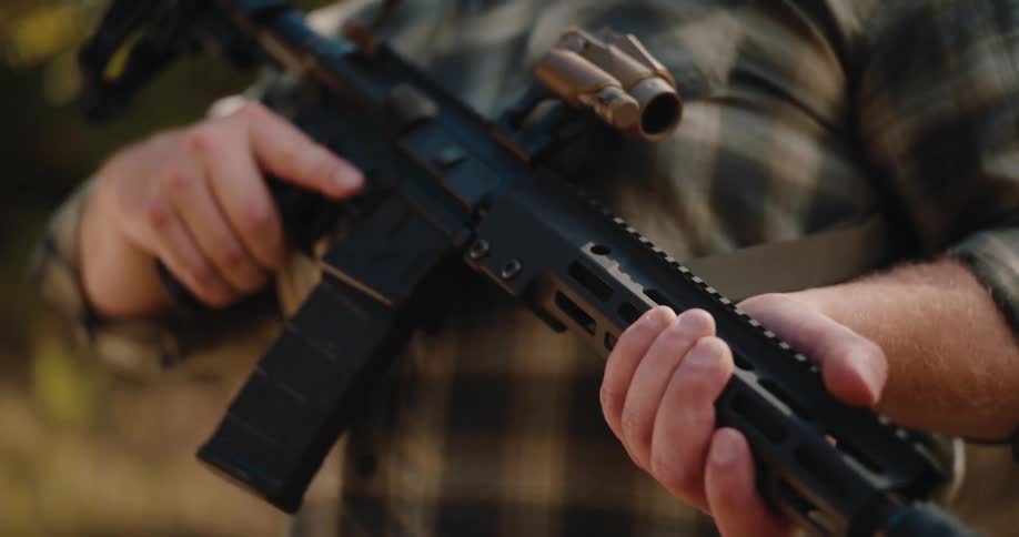 A man grips his rifle while standing in the wilderness under a bright sunlight