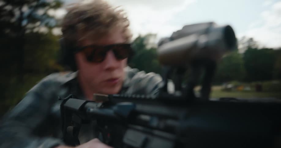 Man wearing sunglasses firing a gun in a field