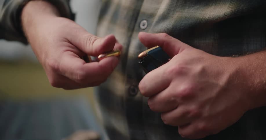 A person slides several individual bullets into a handgun clip