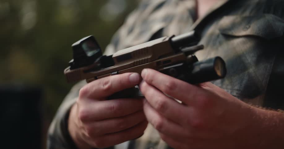 A man holding a handgun carefully inspects the weapon