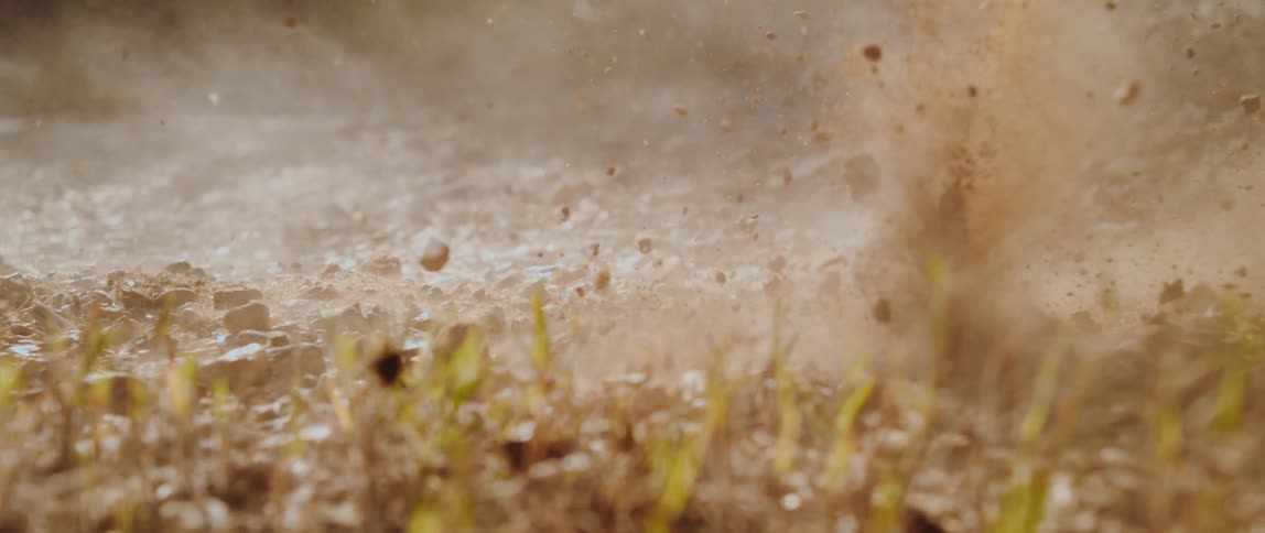 Dirt and rocks erupt from the ground in a sunlit slowmotion burst scattering through the air before settling back down