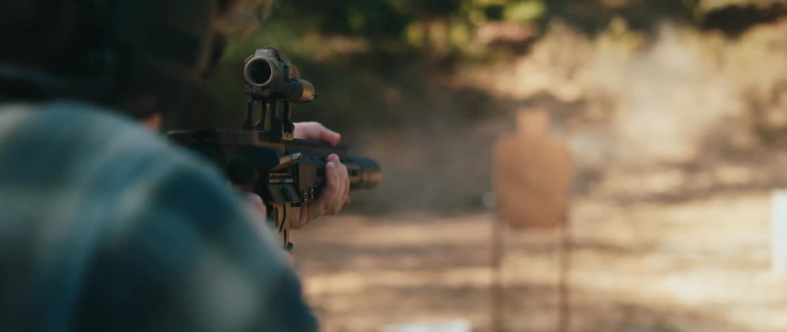 A man in a plaid shirt fires a rifle at a cardboard target on an outdoor range while empty brass casings fly through the air and smoke rises from the barrel in slow motion against a backdrop of trees