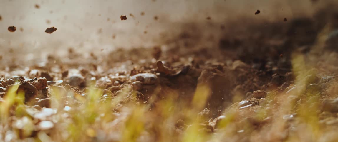 Dirt and pebbles explode upward in a dramatic slow motion close up