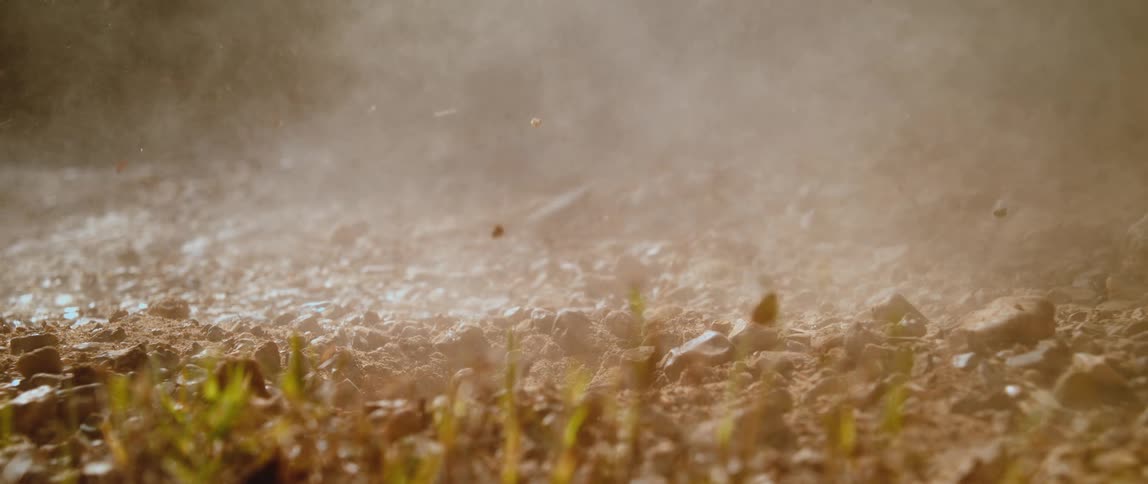 A burst of dirt flying into the air as a large rock hits the ground at midday
