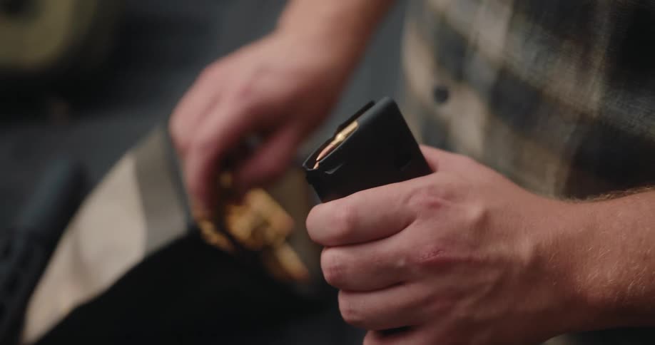 A person stands next to a pickup truck loading bullets into a magazine in an outdoor area