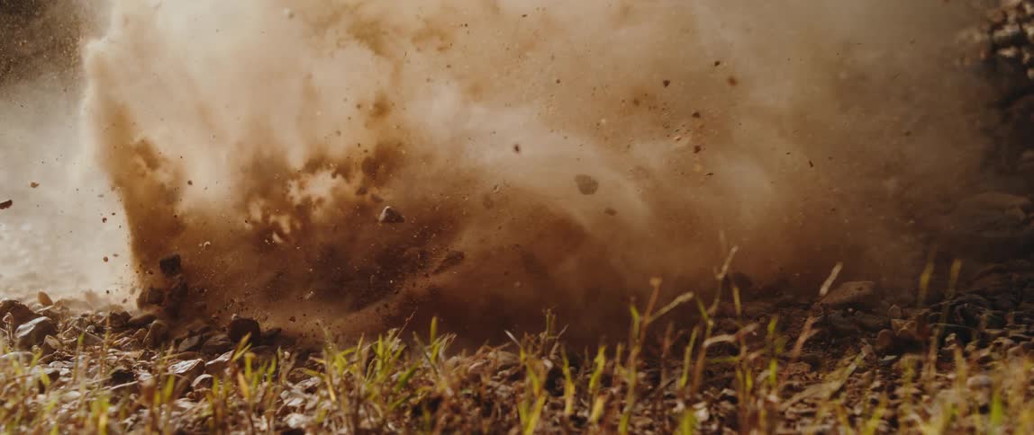 A powerful explosion sends dirt and rocks bursting into the air in a natural outdoor scene