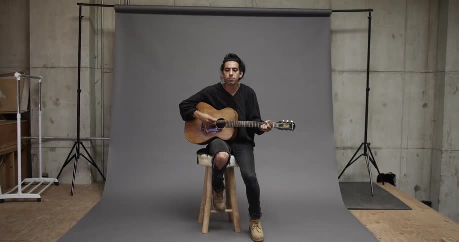 A man sits on a stool and plays guitar