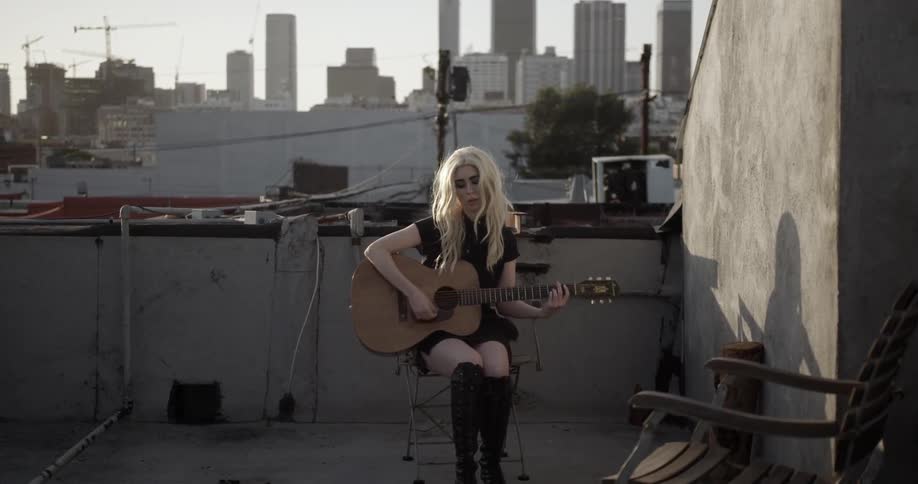 A woman sits on a roof playing guitar by herself