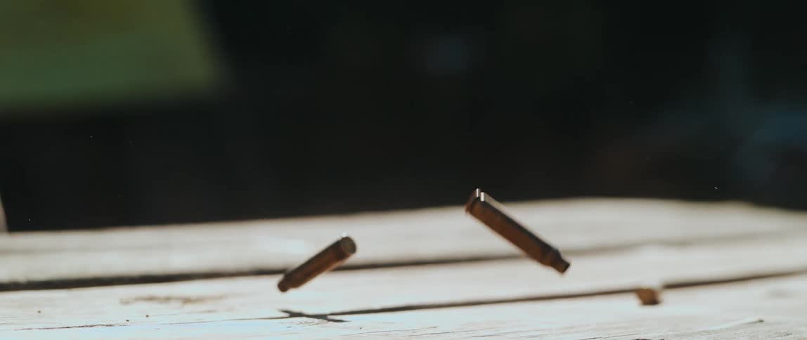 Several spent bullet casings are captured midair and on a wooden surface scattered at different angles as they fall and bounce against a softly blurred background