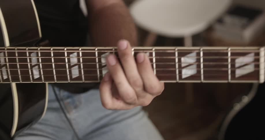 Bearded man strumming a guitar indoors while wearing headphones
