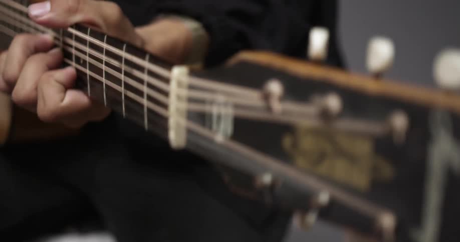 A person plays the guitar wearing a black shirt