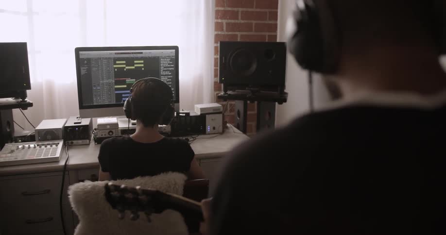 A man plays a guitar while a woman sits at a computer