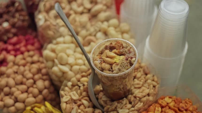 A street vendor pours fresh citrus juice over a mix of nuts and spices in a plastic cup