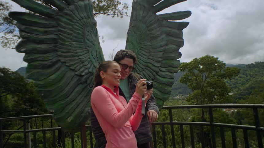 A smiling couple checks photos by sculpted wings with mountains in the background