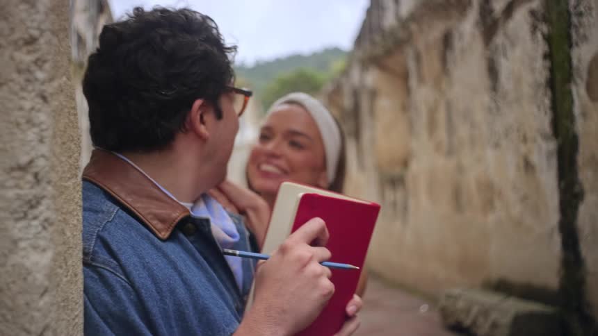 The woman walks up to a man writing in a notebook