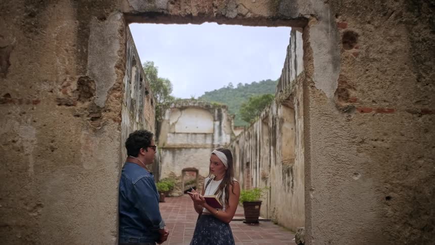 At the top of the frame there is a heavy rectangular stone or concrete beam that spans across the opening this line creates a solid upper border framing the couple and the background ruins