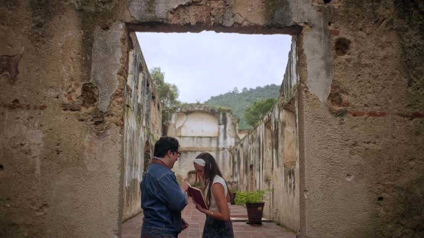 Couple talks beneath a stone arch in historic ruins with an inner courtyard in the background