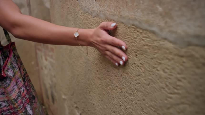 A woman drags her hand flat against a textured wall as she walks past