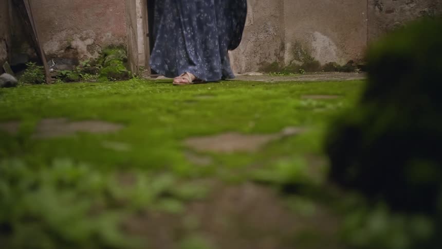 A woman in a long skirt slowly walks along a grassy lawn