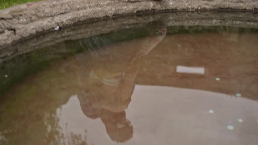 Reflection in a fountain that contains coins shows a man walking over to hug a woman sitting on its edge