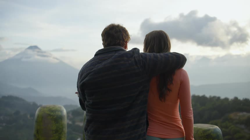 A man has his arm around a woman as the look out upon a valley