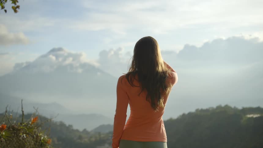 A woman stands overlooking a misty mountainous landscape under bright sunlight