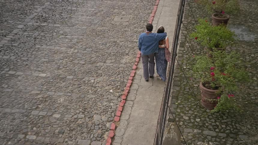A couple walks along a path next to a cobblestone road