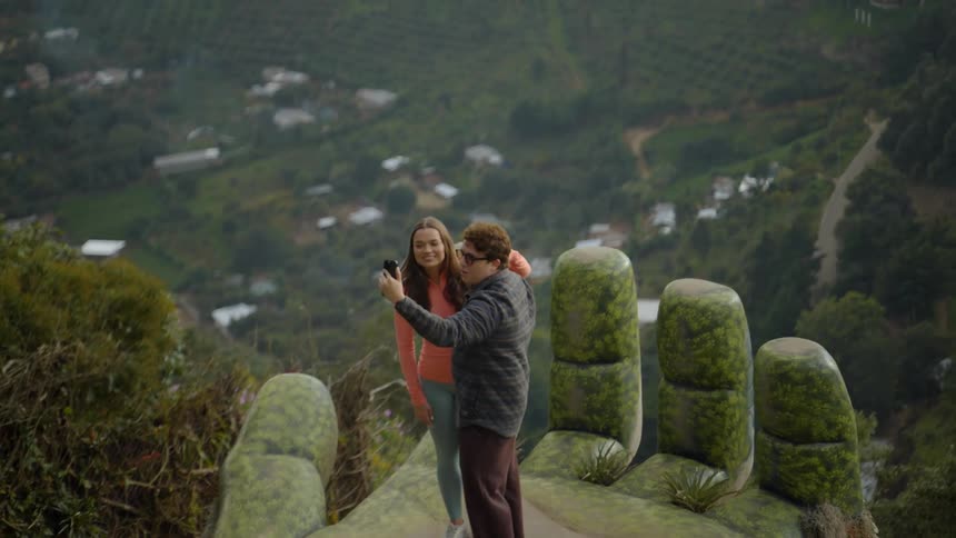 Couple takes a selfie at a high viewpoint overlooking a valley and surrounding greenery