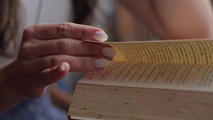 A woman is seated with a book and turns a page while reading it