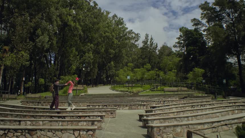 A couple plays and laughs together on stone steps in a park surrounded by tall trees