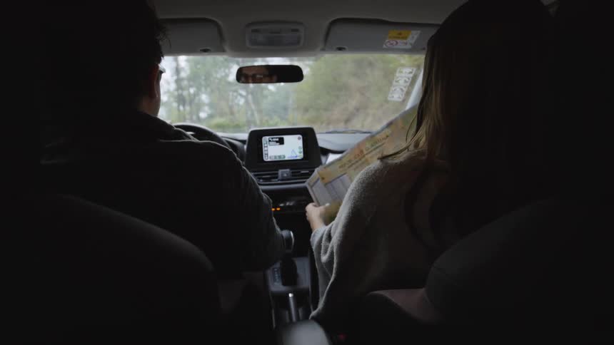 Two people navigate a road trip using a paper map and a digital gps