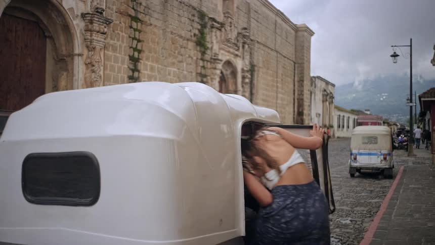 A couple waves from an archway walks down a cobblestone street and gets into a tuk tuk which then drives away