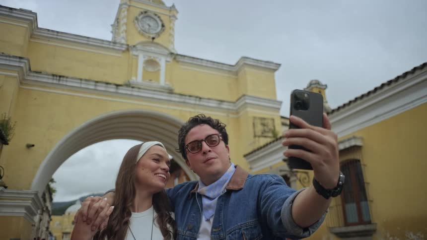 A smiling couple poses for a selfie in front of a historic yellow archway while exploring the city