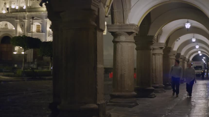 A man and woman walking in a city near some arches