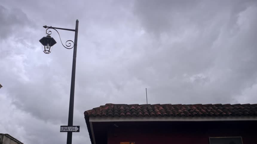 A street lamp on a pole with a sign attached standing beside a building on a cloudy day
