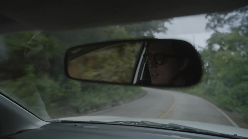 A mans face is seen in the rearview mirror as he drives along a quiet tree lined road