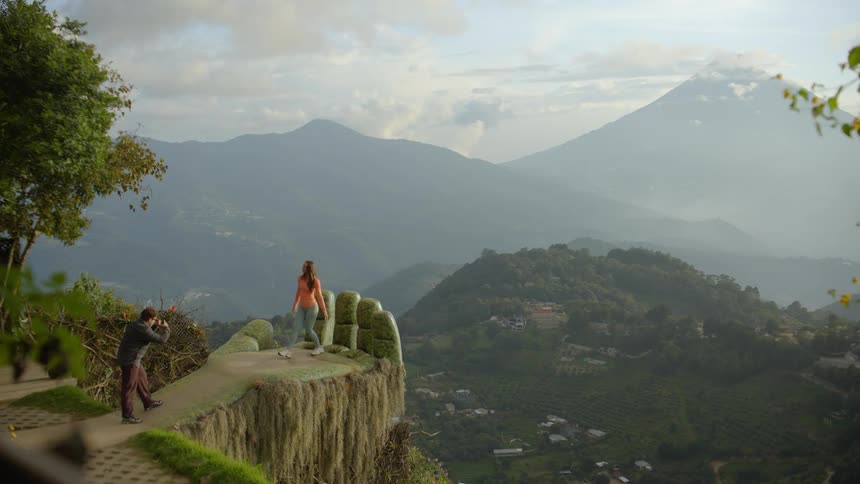Couple taking photos in a monumental area shaped like a hand with mountains in the background