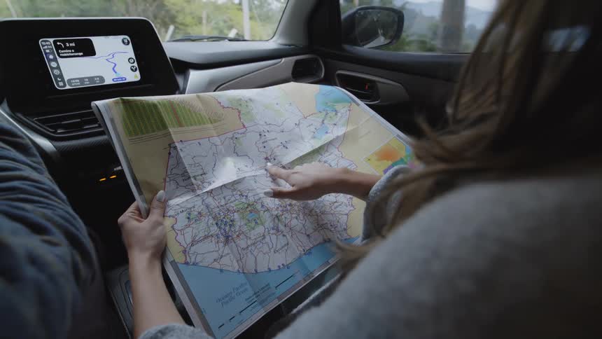 Man drives an automobile and a woman looks at the map spread across her lap