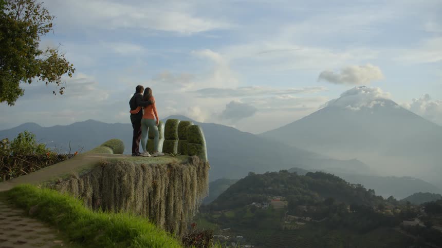 A couple standing side by side hugging on the statue palm at hobbitenango ecopark watching the natural horizon in front of them