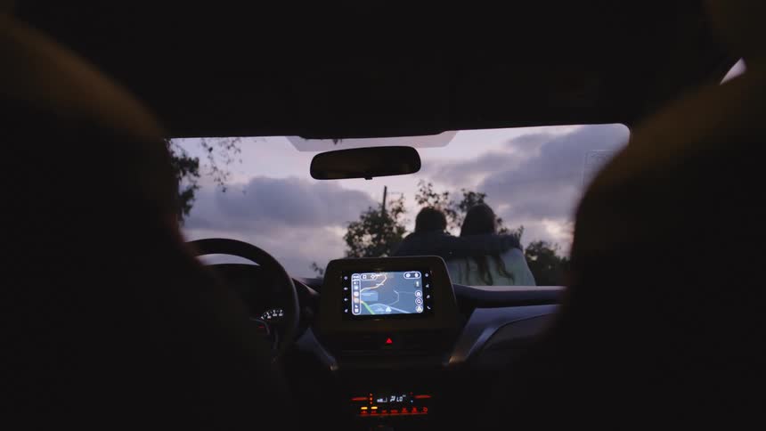 Car interior seen from the back seats with an illuminated center console while two people walk outside at dusk