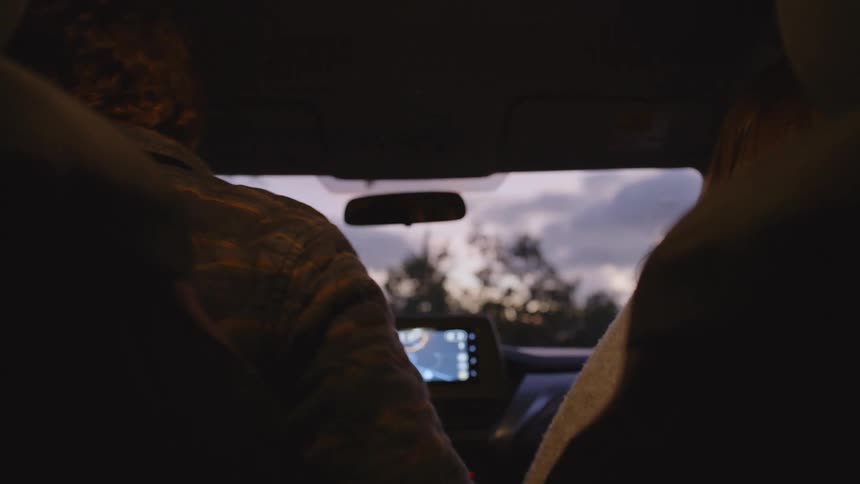 A happy couple shares a laugh as they drive together through the soft glow of dusk