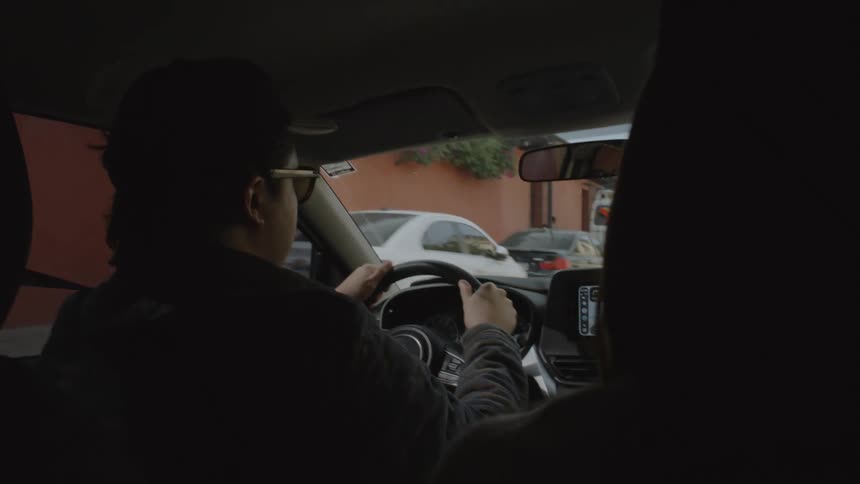 Driver operating a vehicle in an urban area seen from the back seat with the dashboard and road ahead visible
