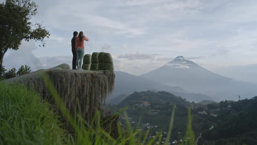 A man and woman stand on a overlook near a tall mountain