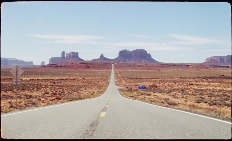 A long straight highway stretches through the desert toward the majestic buttes of monument valley
